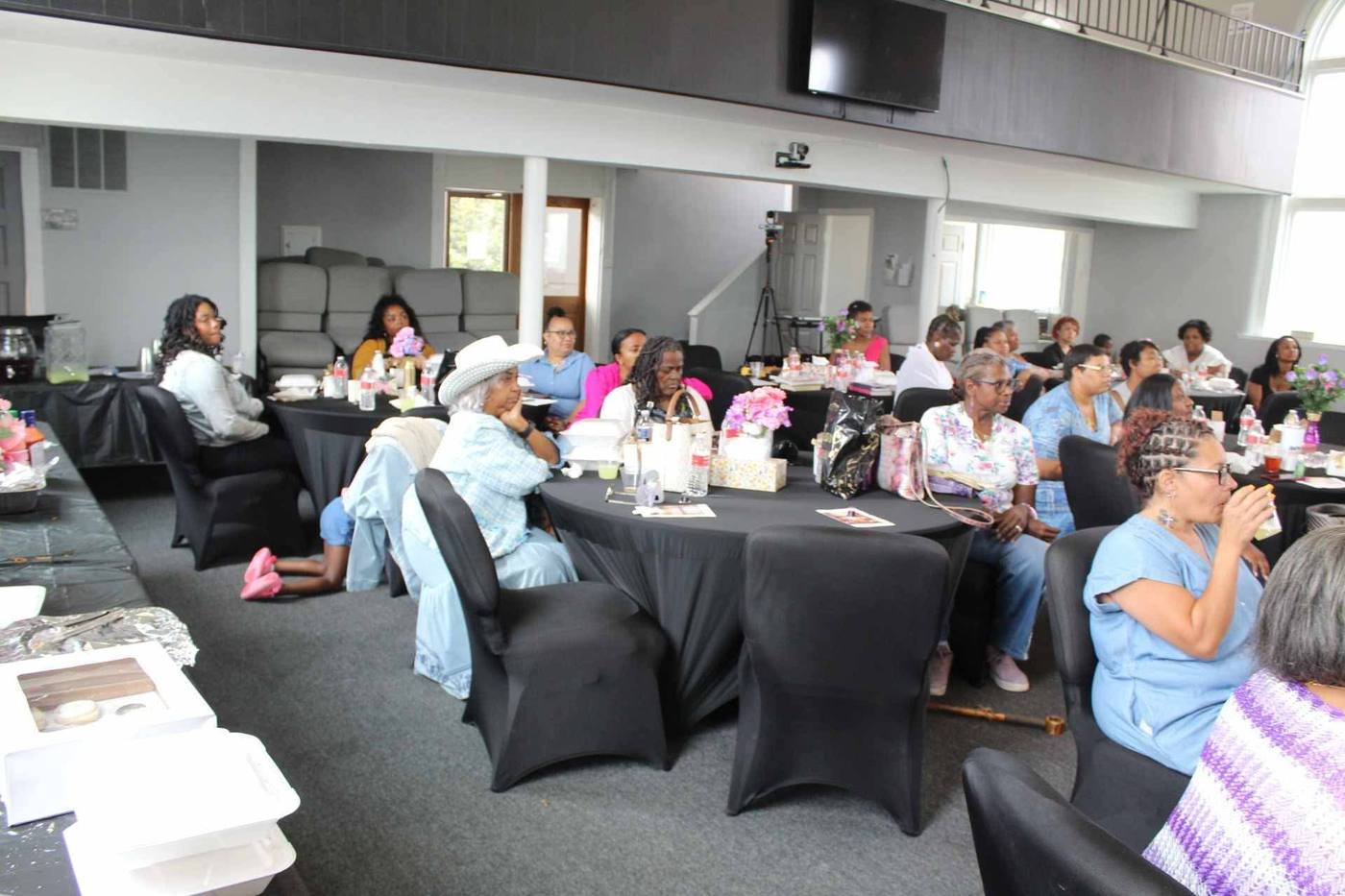 Wide view of the room with women seated at black-draped round tables.