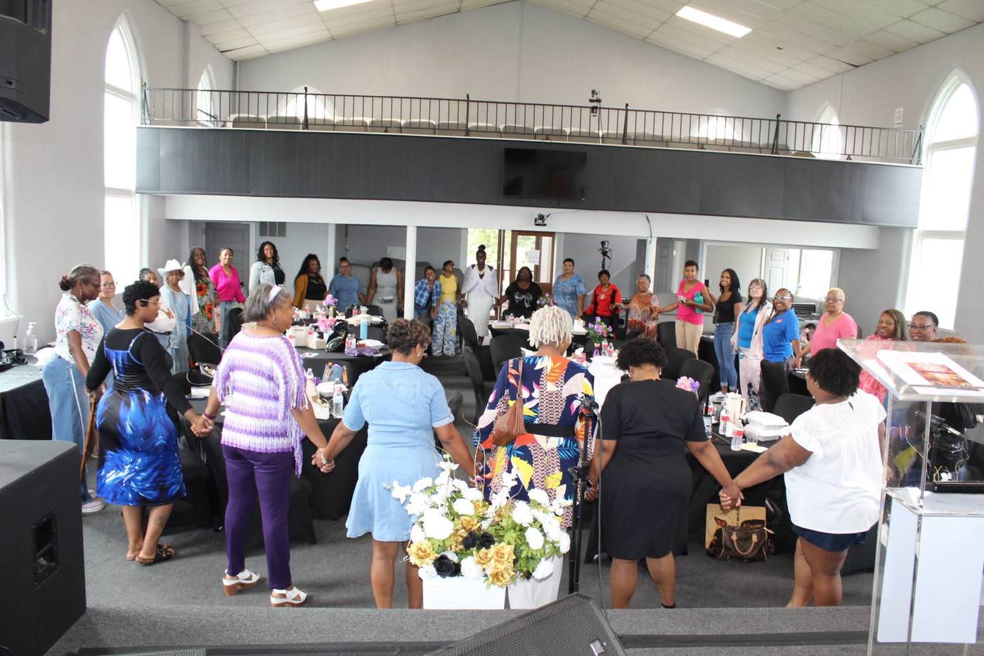 Women joining hands in a large prayer circle around tables in the sanctuary.