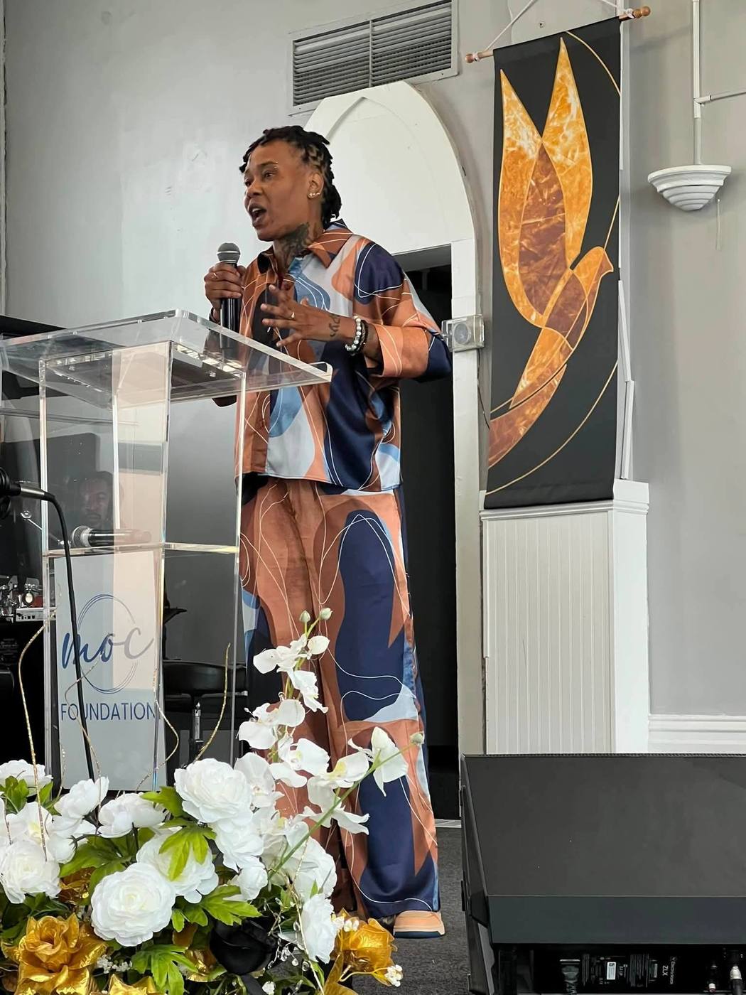 Speaker in a coral and navy patterned outfit at the acrylic podium.