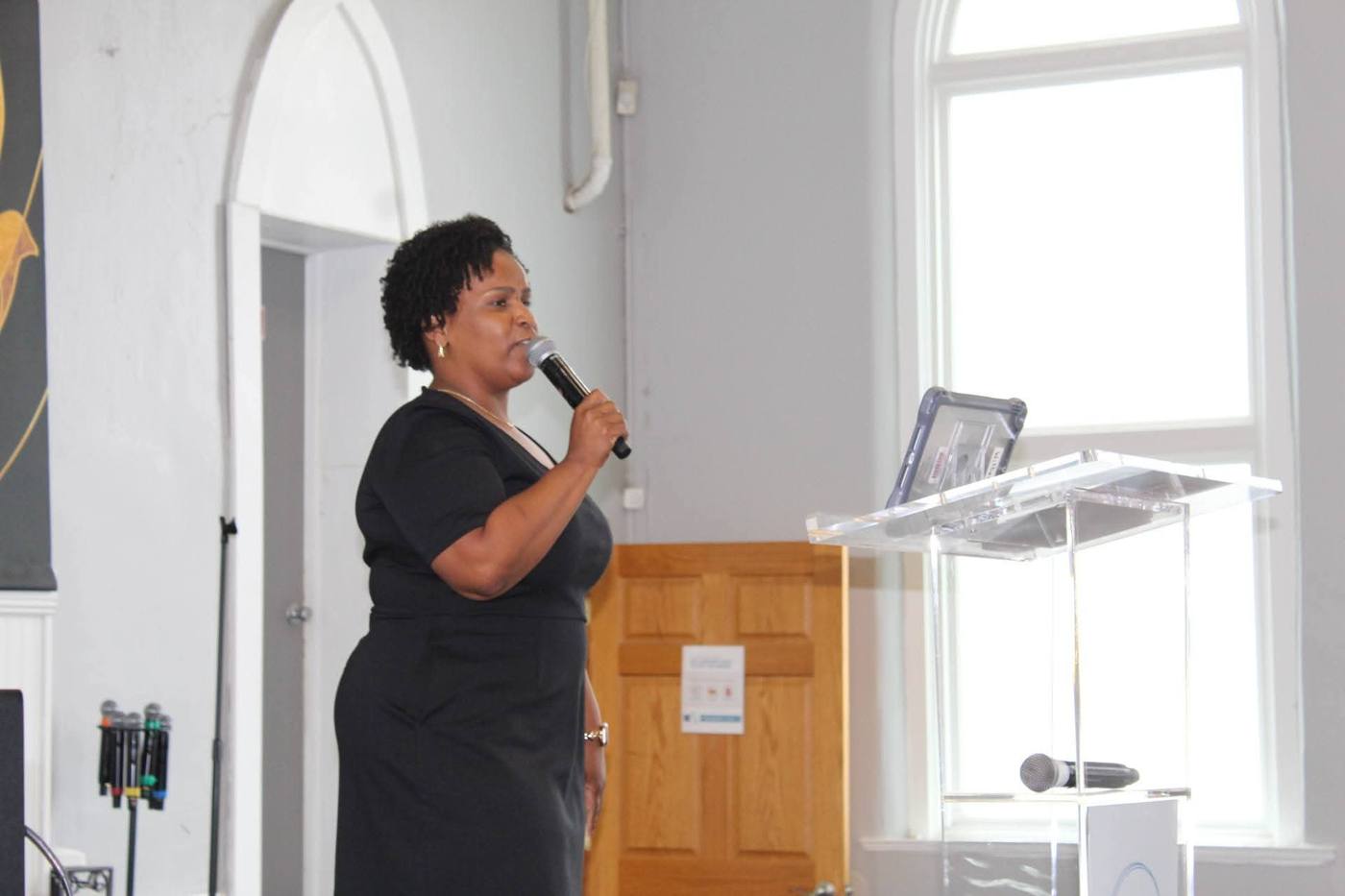 Speaker in a black dress speaking into a microphone beside the podium.